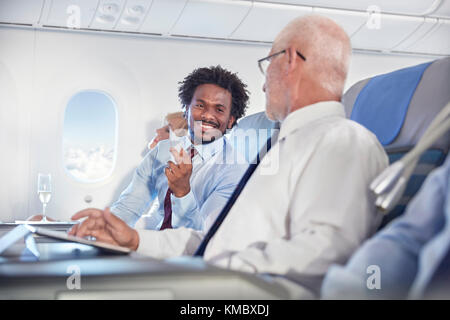 Lächelnde Geschäftsleute tauschen Visitenkarten im Flugzeug aus Stockfoto