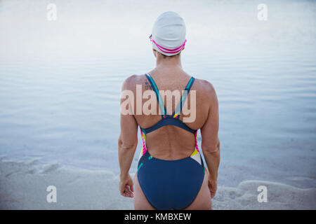 Weibliche Schwimmerin im offenen Wasser, die am Meeresstrand steht Stockfoto