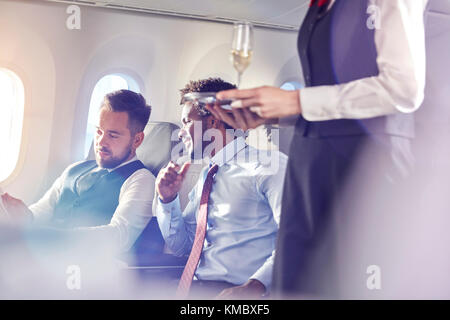 Flight Attendant Champagner an Unternehmer in der ersten Klasse im Flugzeug Stockfoto