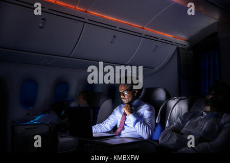 Geschäftsmann, der im Nachtflugzeug am Laptop arbeitet Stockfoto