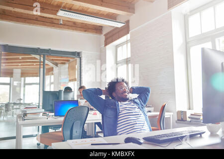 Zuversichtlich Geschäftsmann lehnte sich mit den Händen hinter dem Kopf am Computer Stockfoto