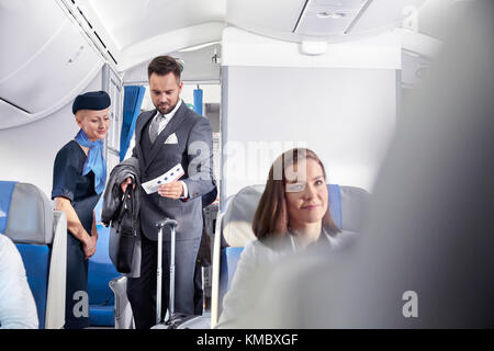 Flugbegleiter hilft Geschäftsmann mit Bordkarte im Flugzeug Stockfoto