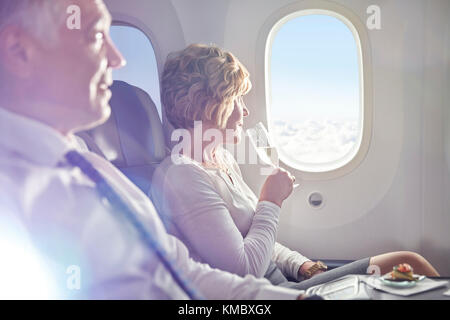 Frau trinkt Champagner in erster Klasse und blickt aus dem Flugzeugfenster Stockfoto