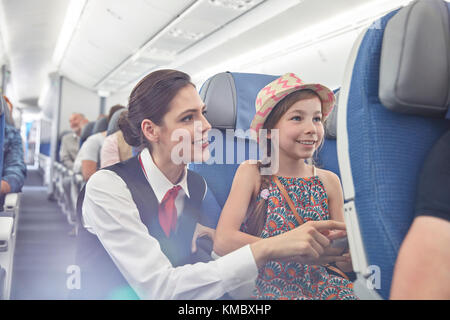 Weibliche Flugbegleiterin hilft Mädchen im Flugzeug Stockfoto