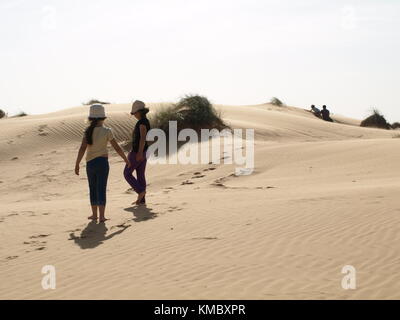 2 Mädchen stehen auf einer Sanddüne mit Vater und seinem Kind im Hintergrund Stockfoto