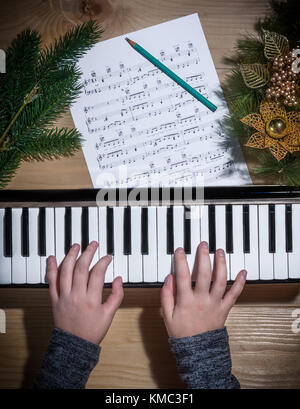 Junge Hände ein Mädchen beim Spielen auf einer Tastatur mit Weihnachtsschmuck auf einem Holztisch Stockfoto