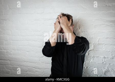 Ein niedergedrückter Mann hält seinen Kopf, während er an Depressionen und Versagen leidet. Verwenden Sie es für Kopfschmerzen, Geldprobleme oder häusliche Gewalt. Stockfoto