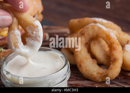 Nahaufnahme der männlichen Hand in weiße Knoblauchsauce gebratene Zwiebelringe tauchen. Stockfoto