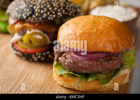 Nahaufnahme eines Sets von drei hausgemachten Mini-Burger mit Rindfleisch aus Marmor und Gemüse auf einem Holzbrett. Stockfoto