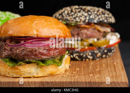 Nahaufnahme eines Sets von drei hausgemachten Mini-Burger mit Rindfleisch aus Marmor und Gemüse auf einem Holzbrett. Stockfoto