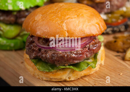 Nahaufnahme eines Sets von drei hausgemachten Mini-Burger mit Rindfleisch aus Marmor und Gemüse auf einem Holzbrett. Stockfoto