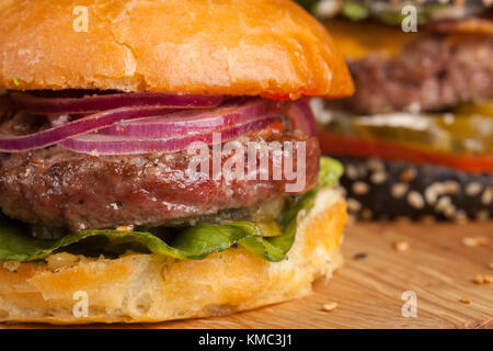 Nahaufnahme eines Sets von drei hausgemachten Mini-Burger mit Rindfleisch aus Marmor und Gemüse auf einem Holzbrett. Stockfoto