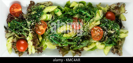 Frische gesunde Gemüse Salat mit Kirschtomaten, Avocado, Gurke, grüne Blätter auf weiße horizontale Platte, Top View, close-up Stockfoto