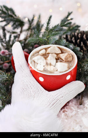 Frau oder des Mädchens behandschuhten Hand eine Tasse heiße Schokolade mit Marshmallows. Extrem flache Tiefenschärfe mit selektiven Fokus auf Kakao. Stockfoto