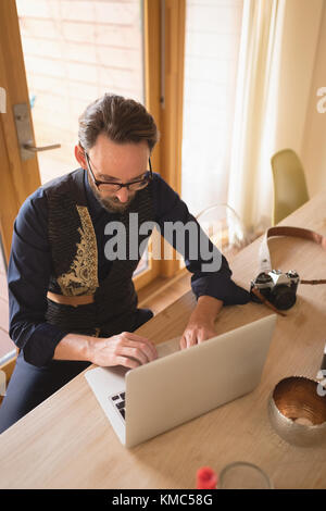 Mann in gut gekleideter Kleidung mit Laptop auf Esstisch Stockfoto