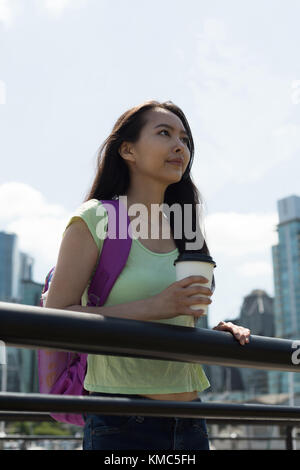 Asiatische Frau mit einer Kaffeetasse, die in der Nähe des Geländer steht Stockfoto