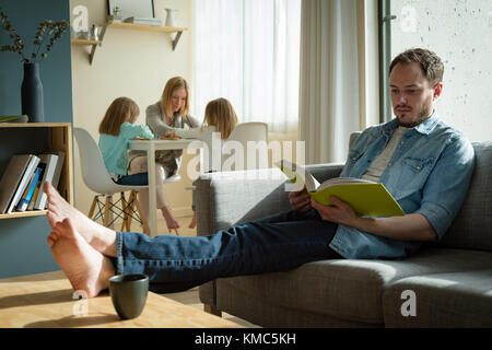 Vater liest ein Buch, während Mutter ihren Kindern im Studium hilft Stockfoto
