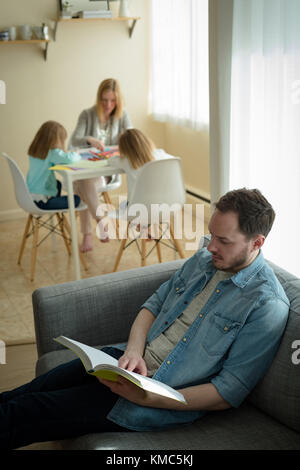 Vater liest ein Buch, während Mutter ihren Kindern im Studium hilft Stockfoto
