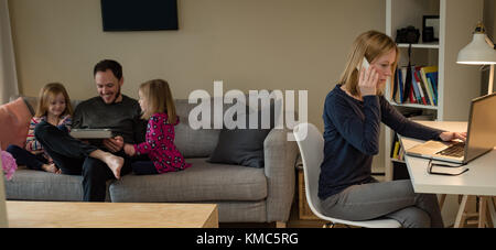 Mutter verwendet Laptop, während Vater und Töchter ein digitales Tablet verwenden Stockfoto