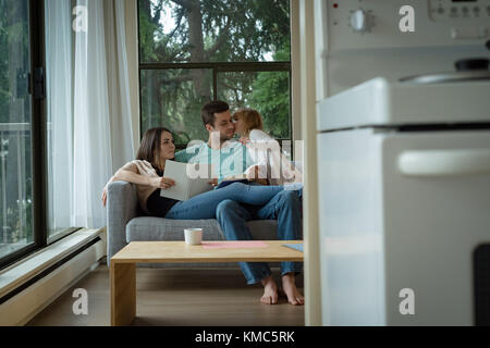 Mutter und Vater lesen Buch, während Tochter ihren Vater küsst Stockfoto
