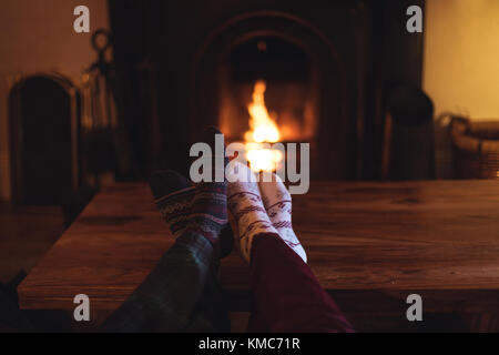 Paar Füße in gestrickten Wollsocken, die sich in der Nähe des brennenden Kamins erwärmen Stockfoto
