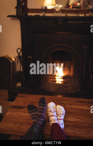 Paar Füße in gestrickten Wollsocken, die sich in der Nähe des brennenden Kamins erwärmen Stockfoto