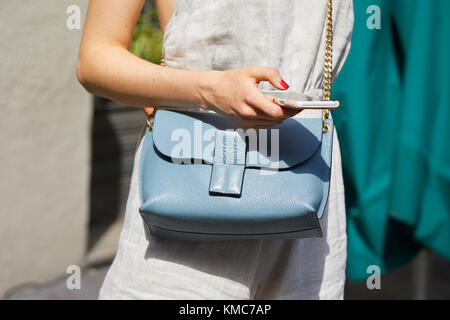 MAILAND - 23. SEPTEMBER: Frau mit hellblauer Ledertasche Loewe mit goldener Kette und Blick auf das Smartphone vor der Blumarine Fashion Show, der Milan Fashion Week Stockfoto