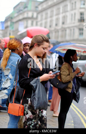 Junge kaukasier Frau Sie Ihr Smartphone während der Wartezeit Straße in London, England, UK zu überqueren Stockfoto