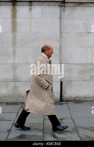 Kaukasische Mann mit Trenchcoat mit Händen in den Taschen zu Fuß über den Trafalgar Square, London, England, Großbritannien Stockfoto