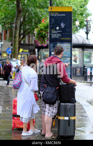 Der Mann und die Frau mit Reisegepäck auf Karte auf öffentliche Information Board im West End, London, England, Großbritannien Stockfoto