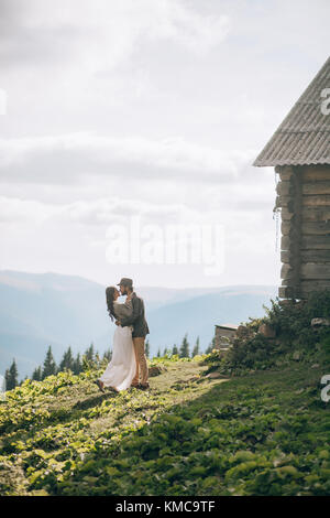 Brautpaar stand in der Nähe der Holzhütte und Hug während der Flitterwochen in den Karpaten. Stockfoto