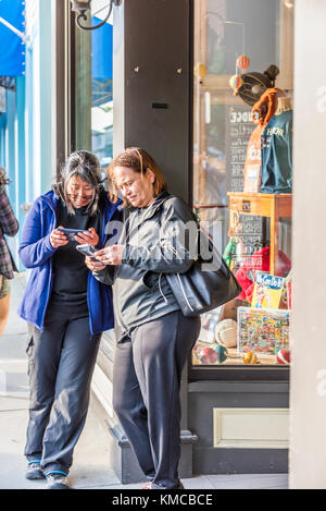 Bar Harbor, USA - 8. Juni 2017: Zwei ältere Frauen stehen am Sommerabend im Dorf Maine und schauen sich Telefone an Stockfoto