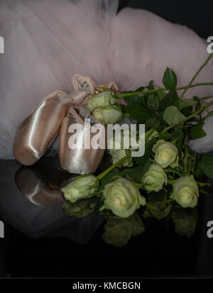 Satin Ballet Shoes, rosa Tutu und rosa Blüten auf schwarzem reflektierenden Hintergrund Stockfoto