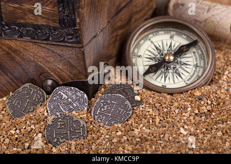 Alte Münzen auf Sand mit Schatzkarte, Kompass und Kasten im Hintergrund Stockfoto