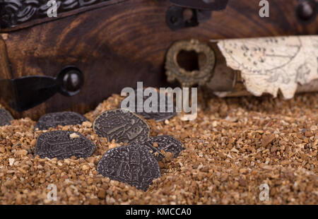 Alte Münzen auf Sand mit Schatzkarte und Kasten im Hintergrund Stockfoto