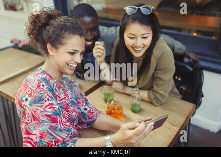 Junge Freundinnen mit Smartphone im Bürgersteig-Café Stockfoto