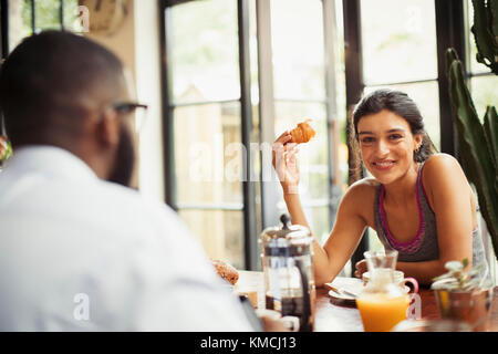 Portrait lächelnde junge Frau genießt Croissant und Kaffee im Café Stockfoto