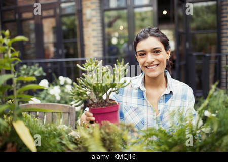 Portrait lächelnde junge Frau im Garten mit Topfpflanzen auf der Terrasse Stockfoto