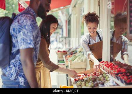 Arbeiter hilft dem Paar beim Einkaufen von Obst auf dem Bürgersteig im Laden Stockfoto