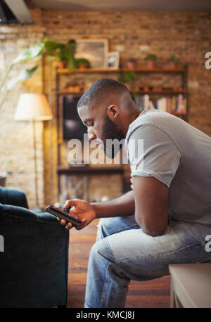 Junger Mann SMS mit Smartphone im Wohnzimmer Stockfoto