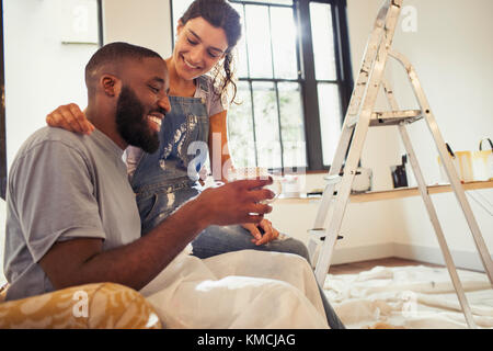 Liebevolles junges Paar trinkt Kaffee und malt Wohnzimmer Stockfoto