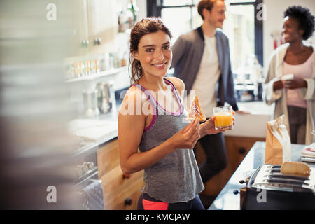 Portrait lächelnde junge Frau, die Toast isst und Orangensaft trinkt In der Küche Stockfoto