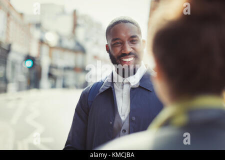 Lächelnder Geschäftsmann im Gespräch mit einem Freund auf der sonnigen städtischen Straße Stockfoto