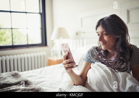 Junge Frau im Bett entspannen, SMS mit Smartphone Stockfoto