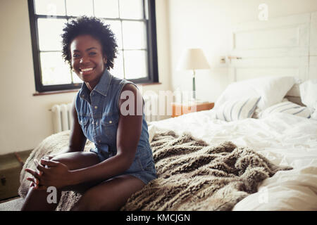 Portrait lächelnde, selbstbewusste Frau auf dem Bett sitzend Stockfoto