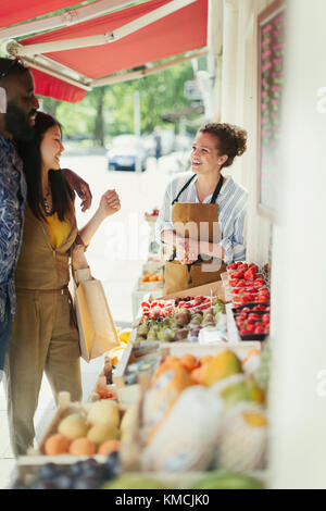 Arbeiterin hilft jungen Paaren beim Einkaufen von Obst auf dem Markt storefront Stockfoto