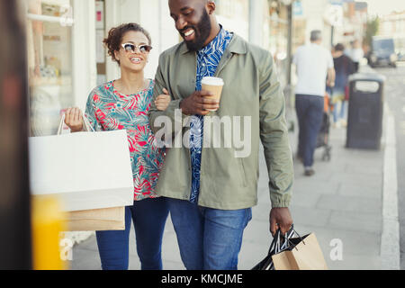 Lächelndes junges Paar mit Kaffee und Einkaufstaschen storefront Stockfoto