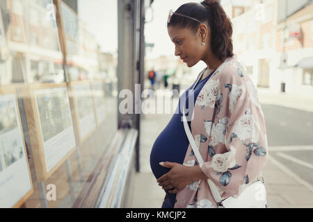 Schwangere Frau beim Durchsuchen von Immobilien-Inserate in städtischen Schaufenster Stockfoto