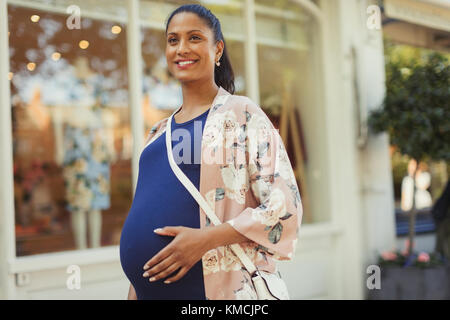 Portrait lächelnde schwangere Frau außerhalb Schaufenster Stockfoto