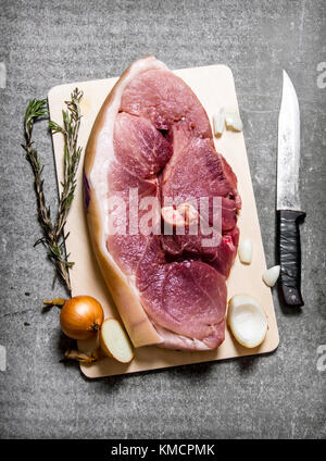 Ein Stück rohes Schweinefleisch mit Gewürzen und einem Messer. Auf den steinernen Tisch. nach oben anzeigen Stockfoto